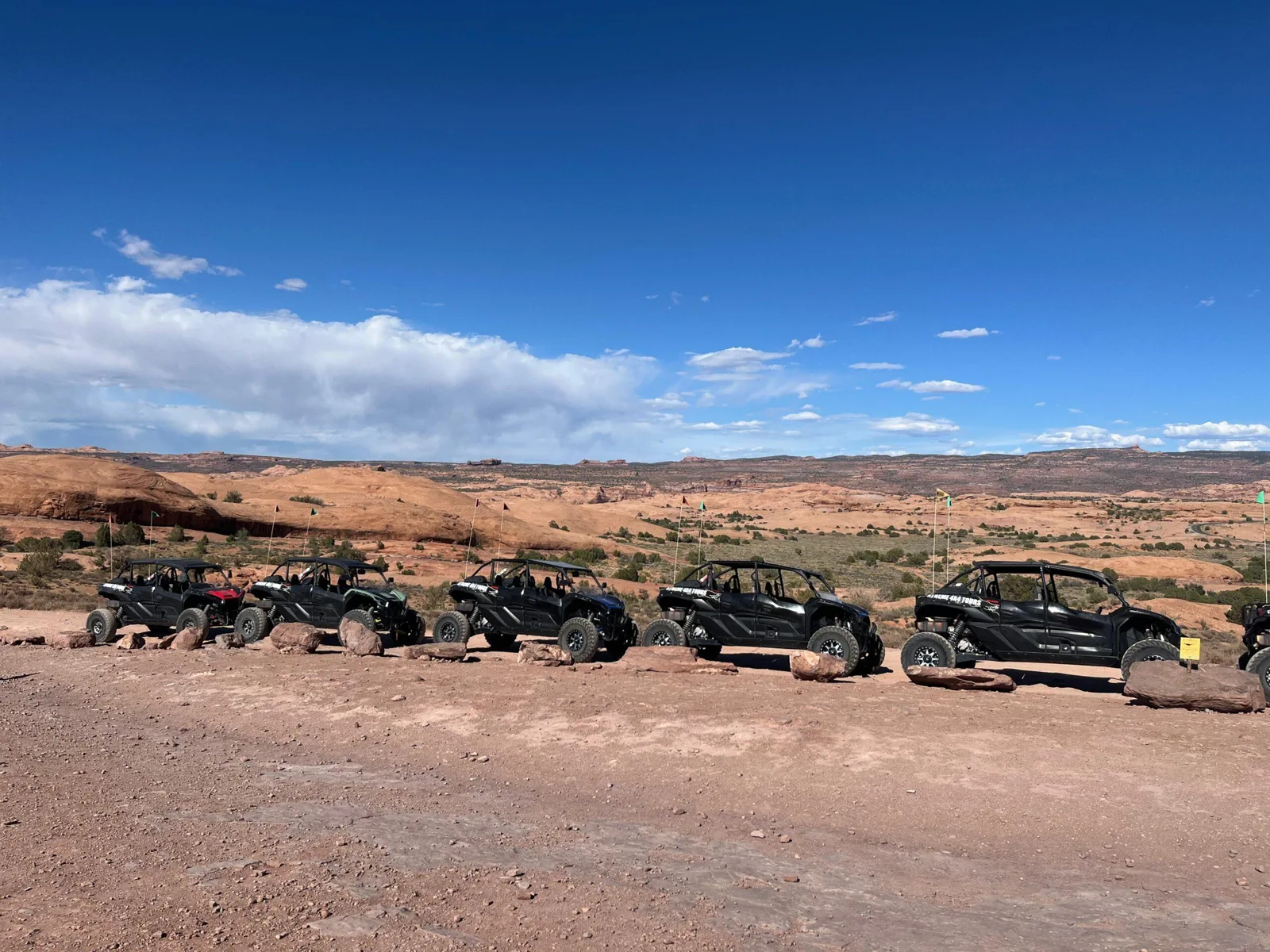 A line of UTVs on open slickrock beneath a blue sky
