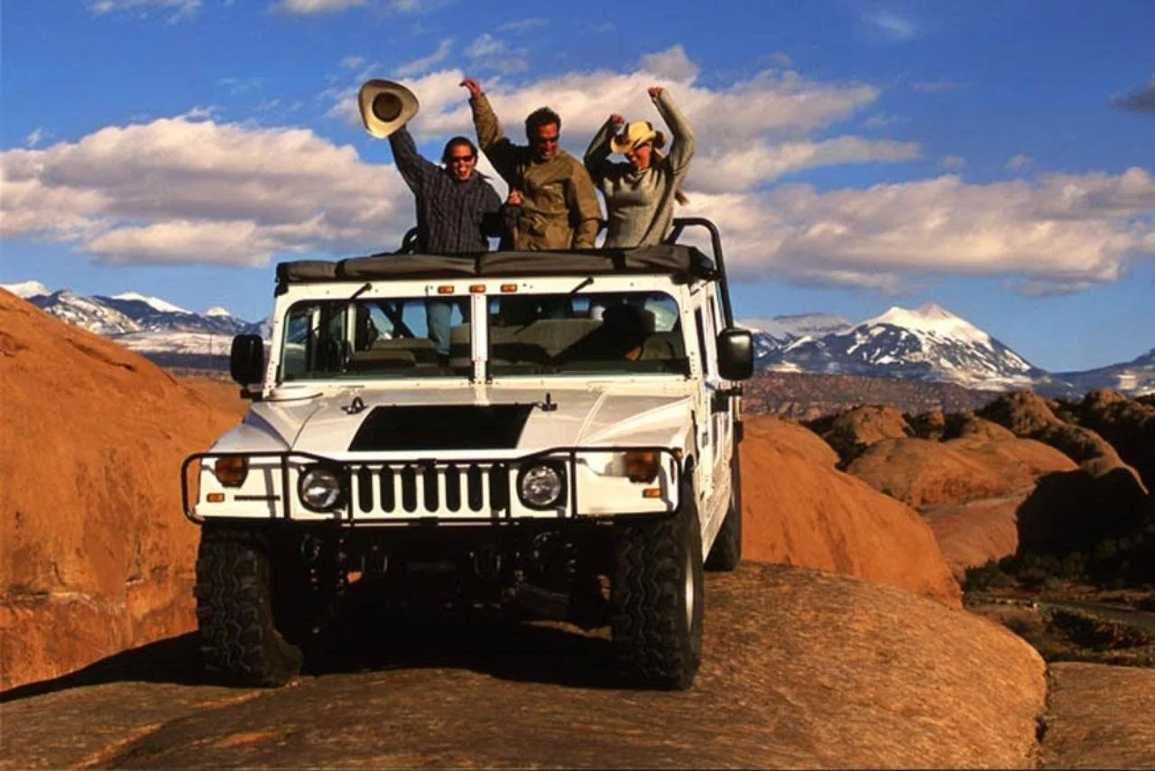 Hummer climbing a sandstone rise with passengers aboard